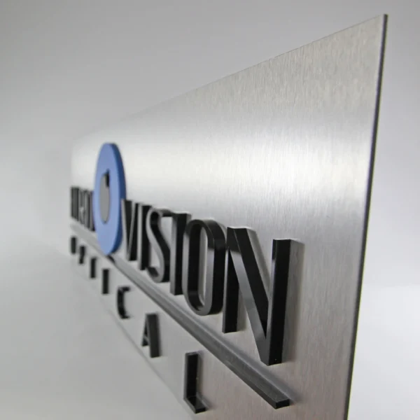 Close-up of a business signage for "Horizon Vision Optical" mounted on a brushed metal panel. The letters are three-dimensional, with "Horizon Vision" in black and a blue circle logo. The sleek, modern design highlights the professional appearance of the signage.